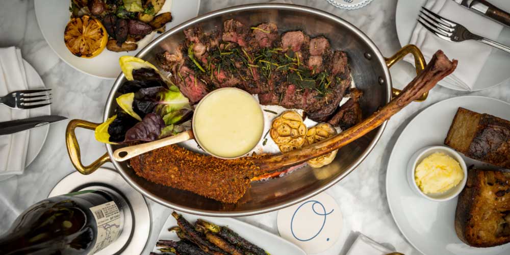 Olivetta - A gourmet meat dish served in a fancy braising dish and surrounded by wine and sides.